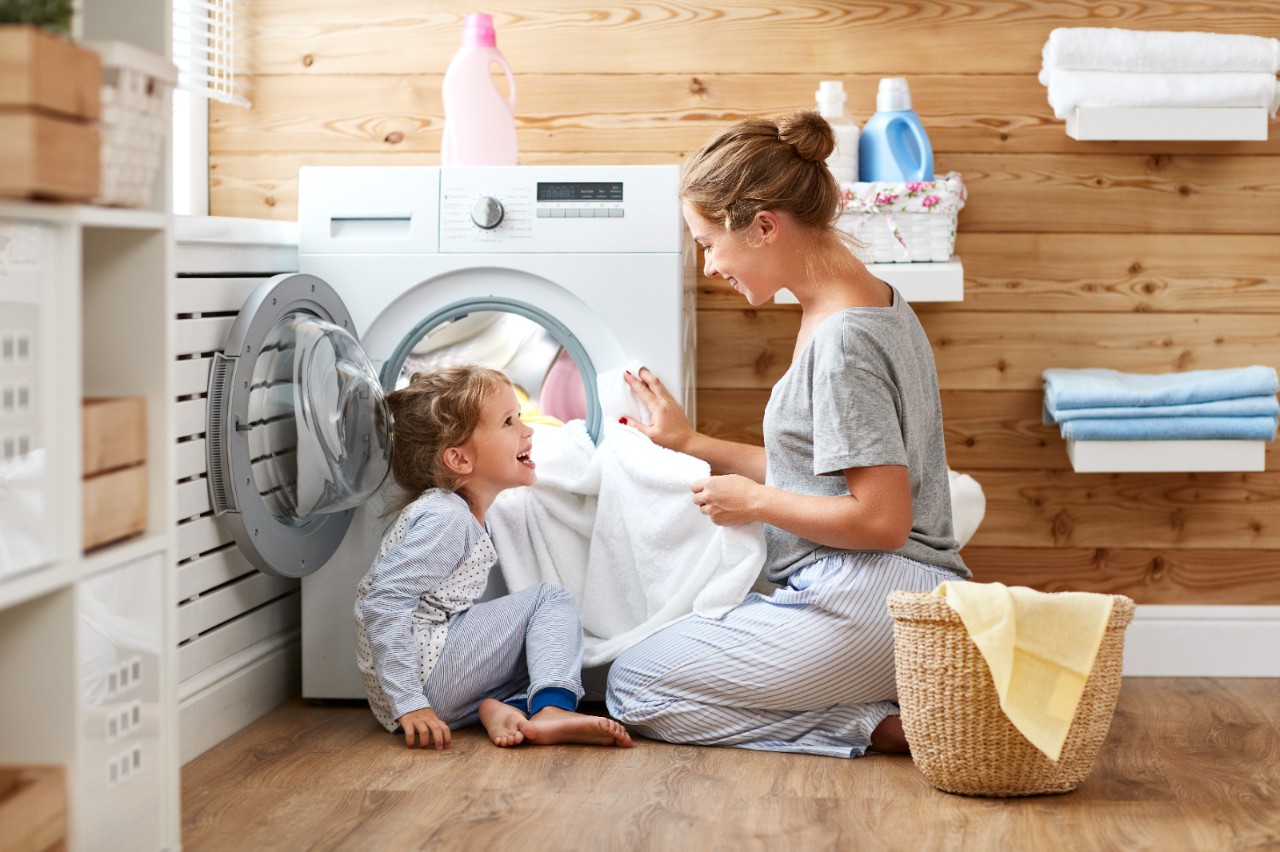 Happy family mother housewife and child daughter in laundry with washing machine