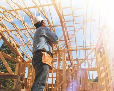 Man in hard hat looking at house frame construction